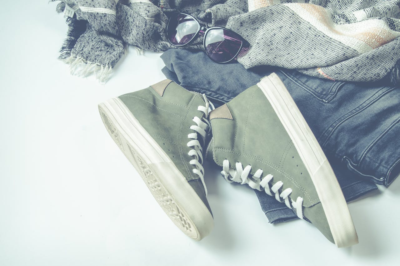 Flat lay of casual fashion items including sneakers, sunglasses, and a shawl.